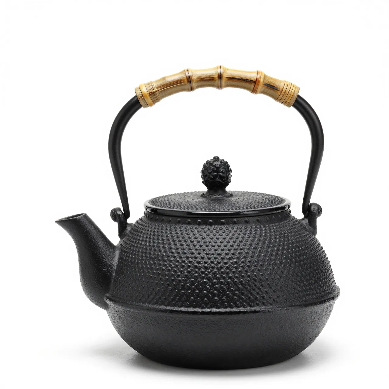 A black hobnail cast iron teapot with bamboo wrapped handle sits isolated on a plain white studio background.