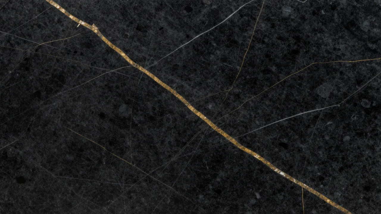 Top view of a polished flat black marble surface with bold gold veins and thin white hairlines filling the frame.