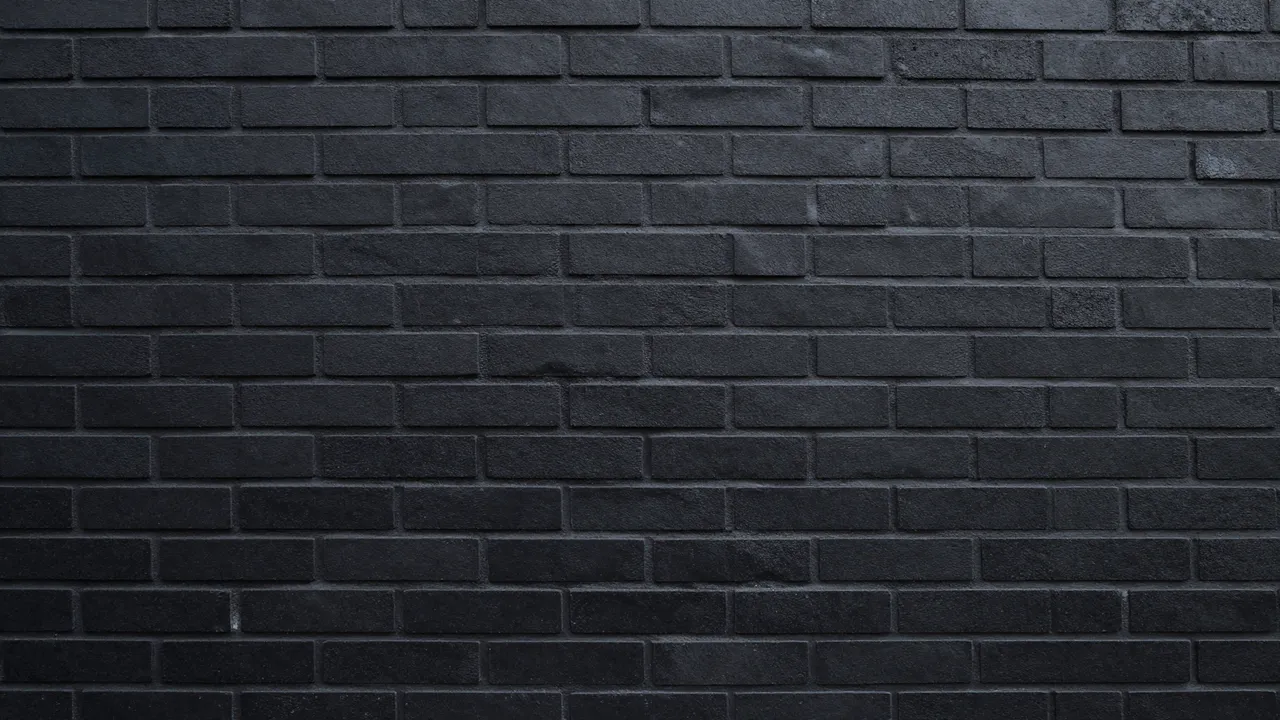Full frame view of a dark black painted brick wall with subtle side lighting and visible mortar lines
