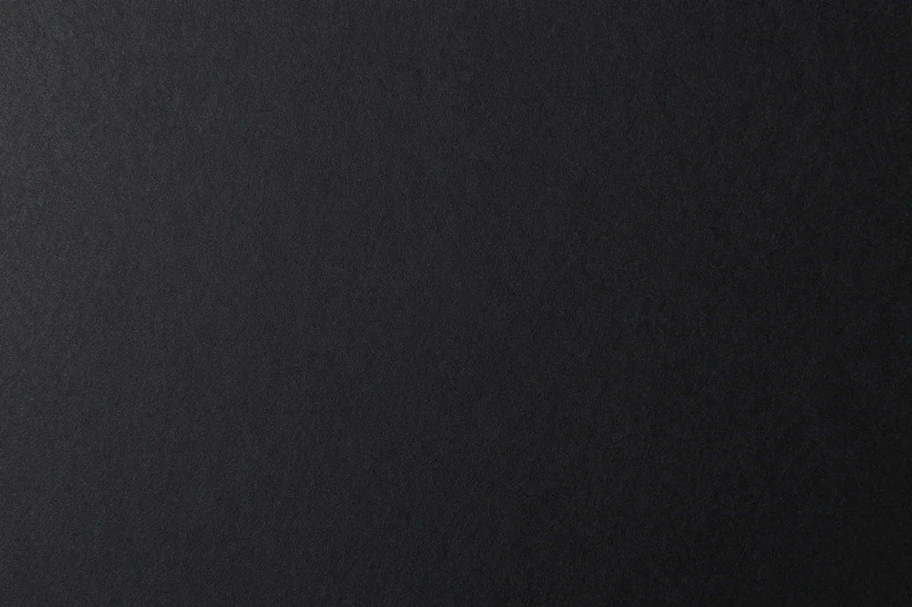 Top view of a matte black paper surface with subtle fine fibrous texture and full copy space