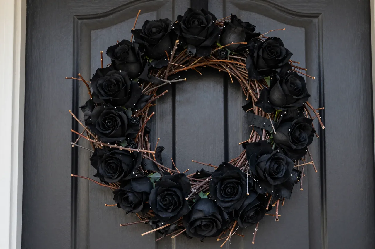 A twig wreath decorated with black roses hangs on a dark gray paneled front door