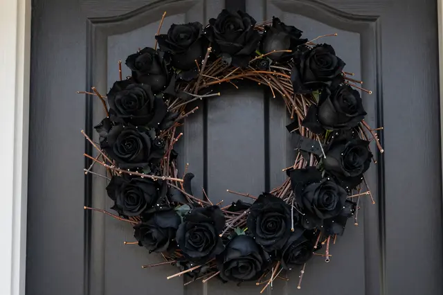 A twig wreath decorated with black roses hangs on a dark gray paneled front door