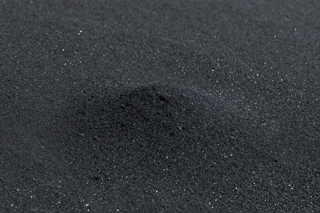 Close-up of fine black volcanic sand dotted with tiny glinting reflective grains