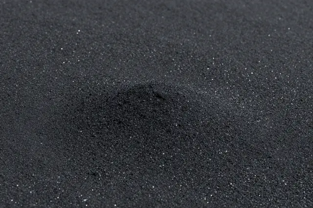 Close-up of fine black volcanic sand dotted with tiny glinting reflective grains