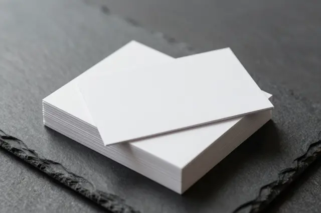 A stack of blank white business cards rests on a dark textured slate surface with soft side lighting.