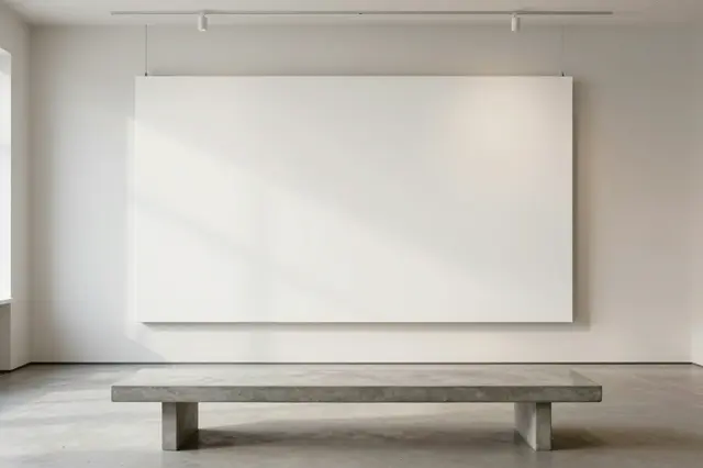 A large blank stretched canvas hangs above a concrete bench in a minimalist bright gallery room