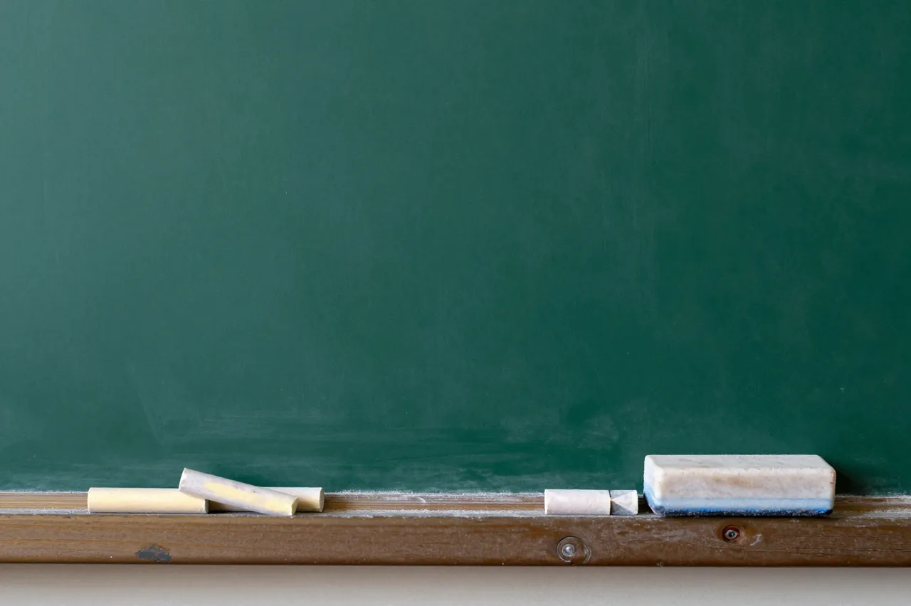 A blank green chalkboard with loose chalk pieces and a chalk eraser resting on its wooden ledge