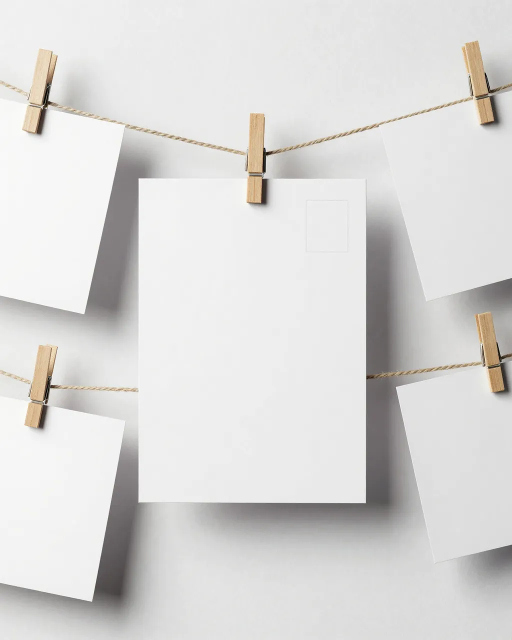 Blank white postcards clipped to twine with wooden clothespins against a plain white wall
