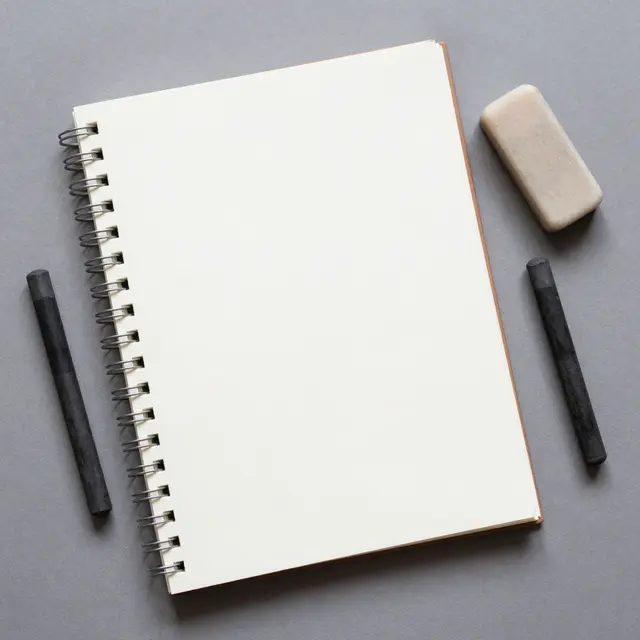 Flat lay of a blank spiral sketchbook, charcoal sticks and eraser on a smooth gray surface