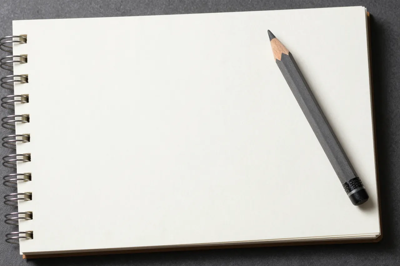 Open spiral-bound sketchbook with a blank page and graphite pencil resting on a dark matte surface
