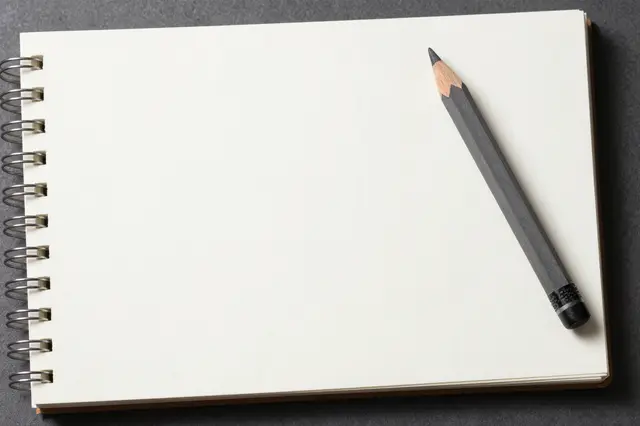 Open spiral-bound sketchbook with a blank page and graphite pencil resting on a dark matte surface
