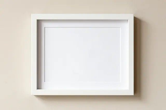 A blank white matted picture frame hangs centered on a smooth beige wall