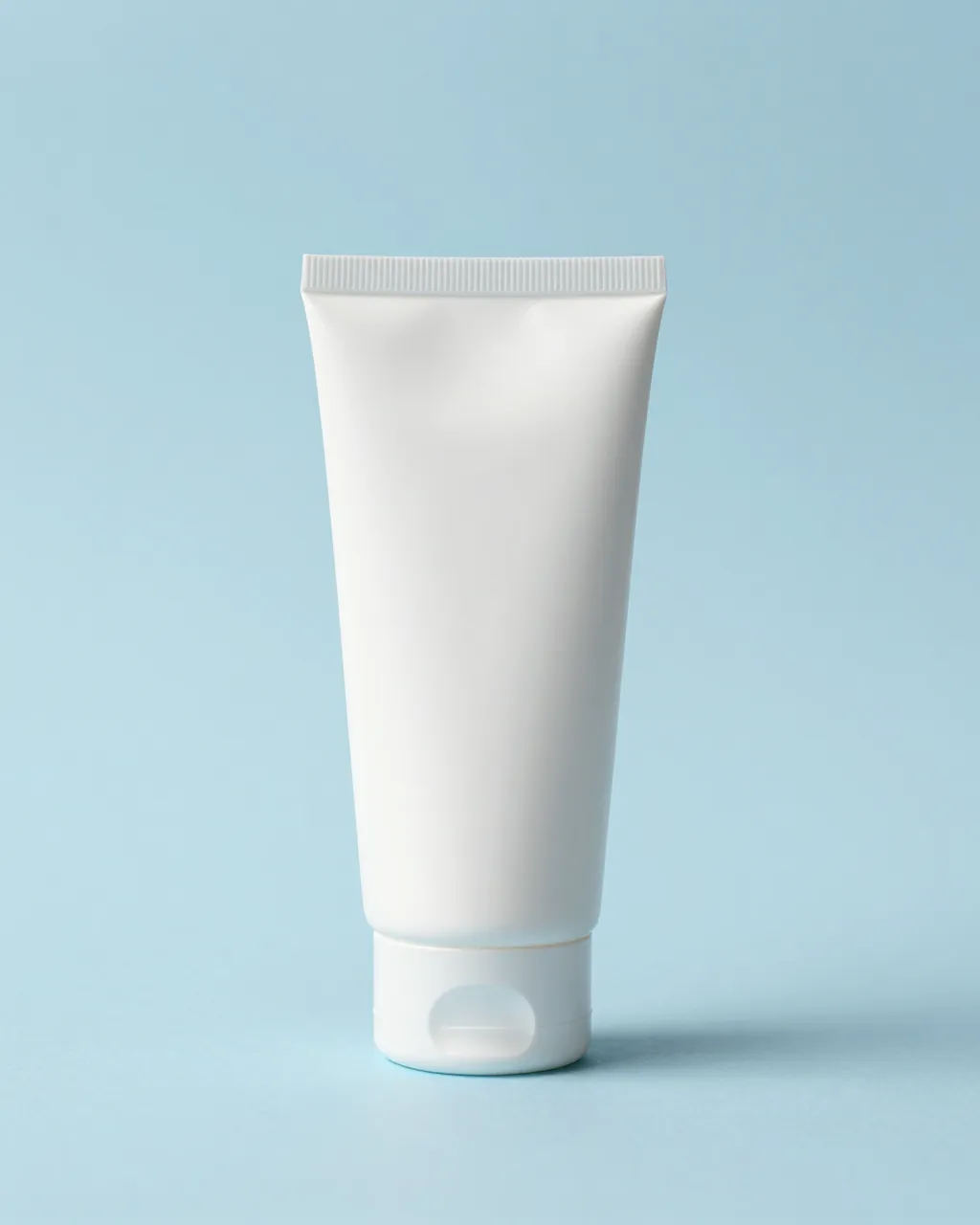 A plain blank white squeeze tube stands upright on a soft pastel blue surface