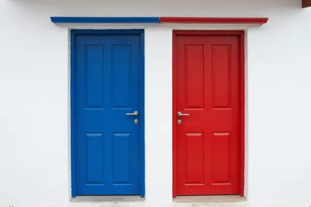 Two adjacent wooden doors, one blue and one red, set into a smooth whitewashed exterior wall.