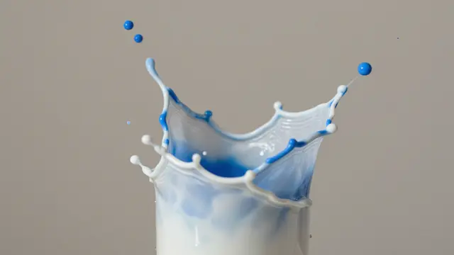 Midair collision of blue and white paint forming a crown-shaped splash against a neutral gray background