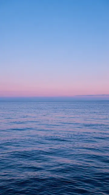 Vertical view of calm rippled sea meeting a soft pink gradient sky at blue hour