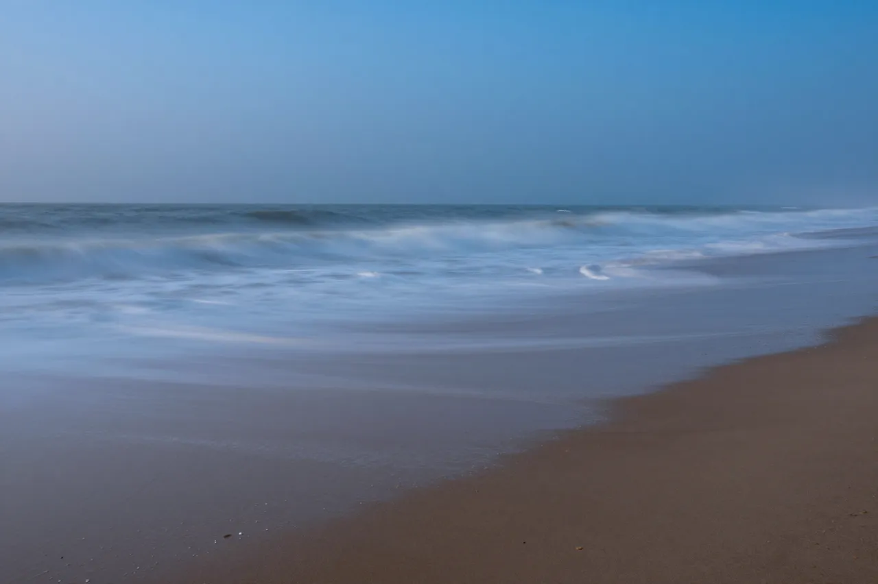 Long exposure view of smooth misty ocean waves rolling onto a sandy beach at blue hour