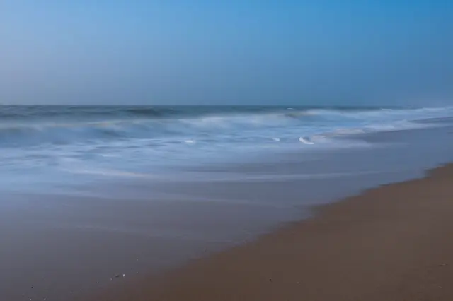 Long exposure view of smooth misty ocean waves rolling onto a sandy beach at blue hour