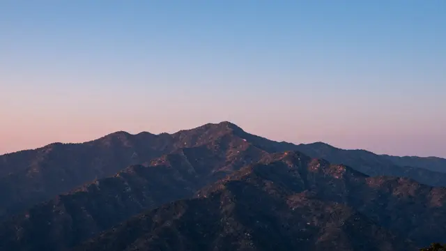 Rugged mountain peaks sit beneath a gradient sky of cool blue and faint pink afterglow at blue hour