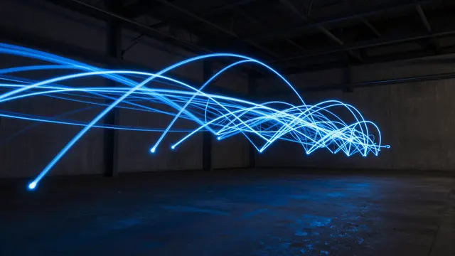 Glowing blue long exposure light trails curve across a dark empty industrial warehouse interior