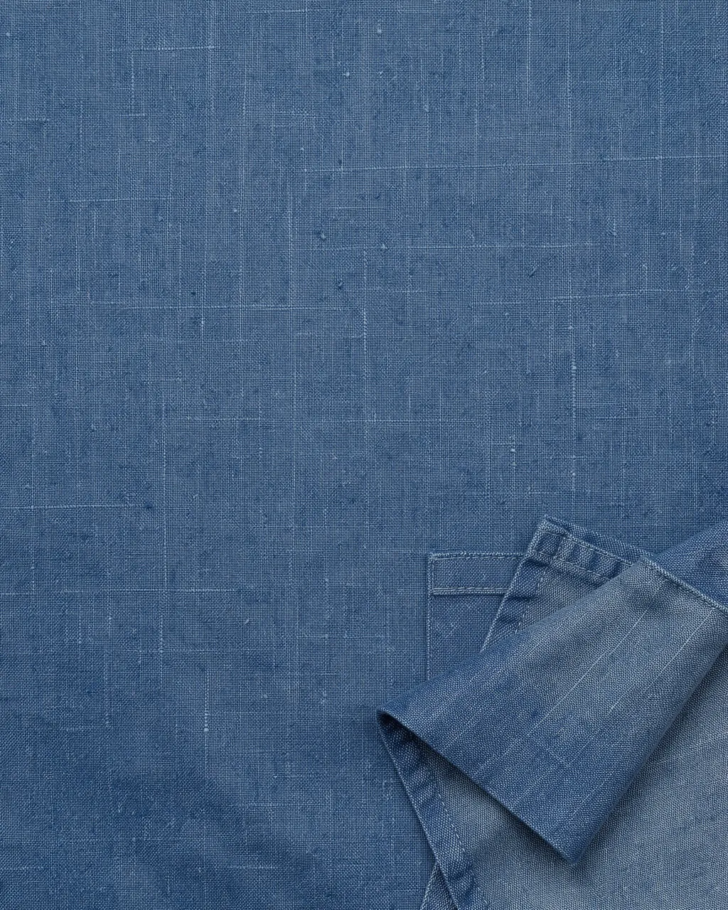 Textured blue denim linen background with a folded fabric detail in the lower right corner and empty copy space above