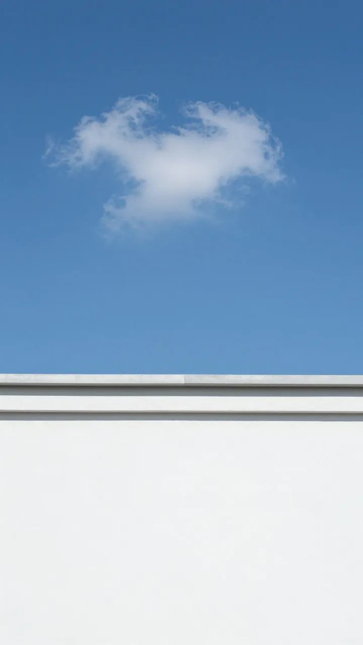 A single wispy cloud floats in a clear bright blue sky above the top edge of a smooth white exterior wall.