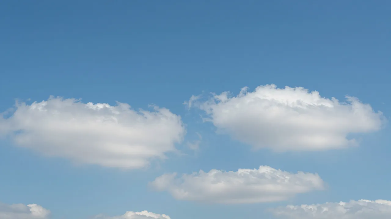 Bright clear blue sky dotted with soft fluffy white cumulus clouds.