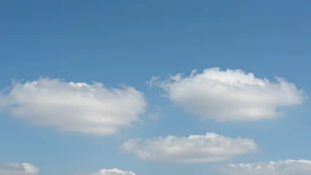 Bright clear blue sky dotted with soft fluffy white cumulus clouds.