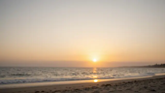 Soft out-of-focus beach scene with a low warm sun setting over gentle ocean waves onto sand