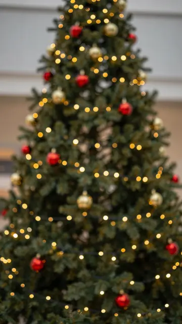 Out of focus decorated Christmas tree with glowing gold fairy light bokeh and red and gold baubles