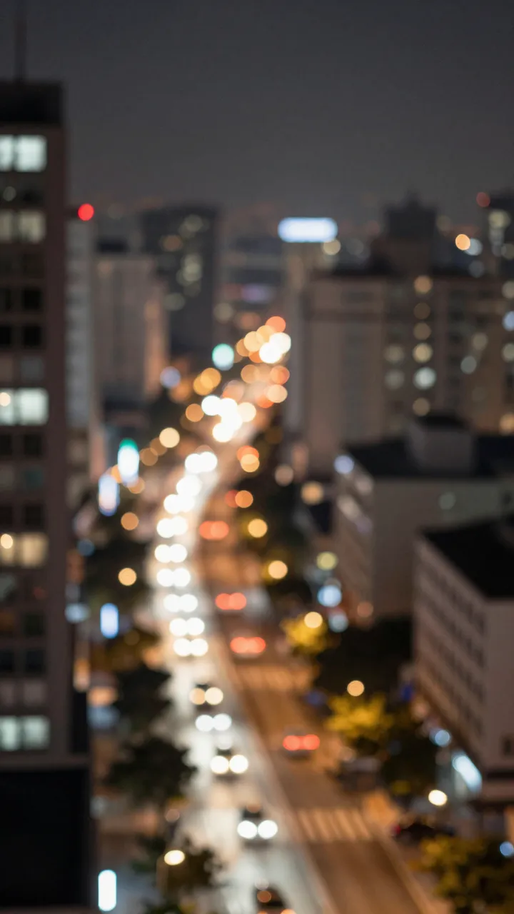 A vertical elevated view of out-of-focus glowing city street lights and buildings after dark