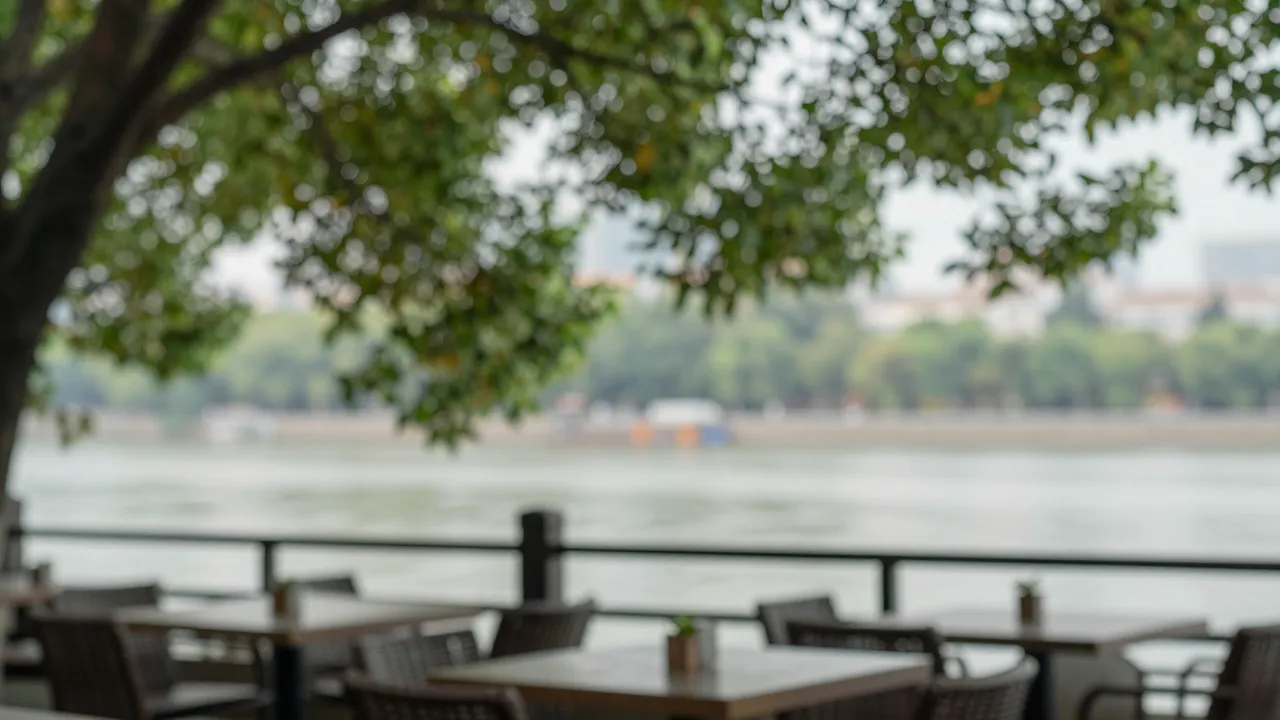 Softly out of focus empty cafe terrace overlooking a calm river under leafy tree branches
