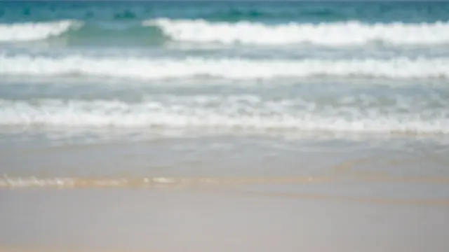 Soft out-of-focus ocean waves roll onto a sandy tropical beach with empty foreground copy space