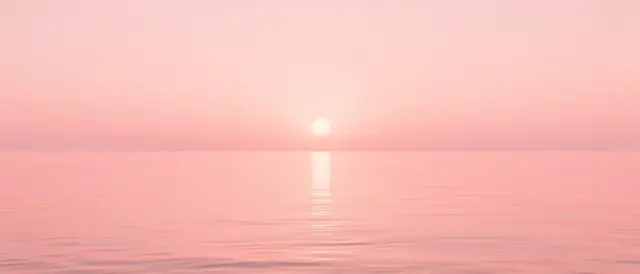 A faint low sun sits over calm pink water beneath a matching soft pink hazy sky