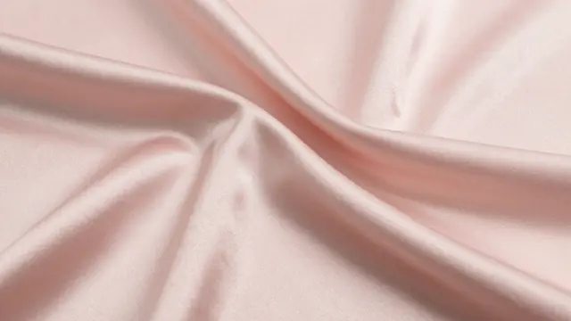 Close-up of soft blush pink satin fabric draped in smooth gentle folds with subtle sheen