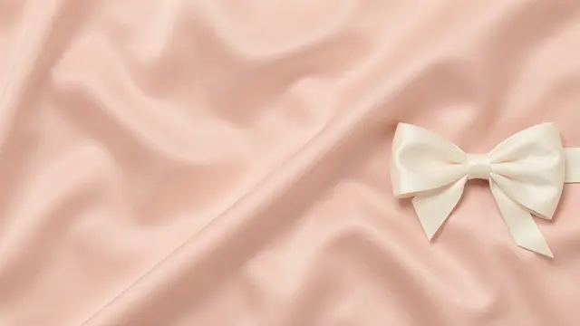 Soft folded blush satin fabric with a cream satin bow positioned on the right side