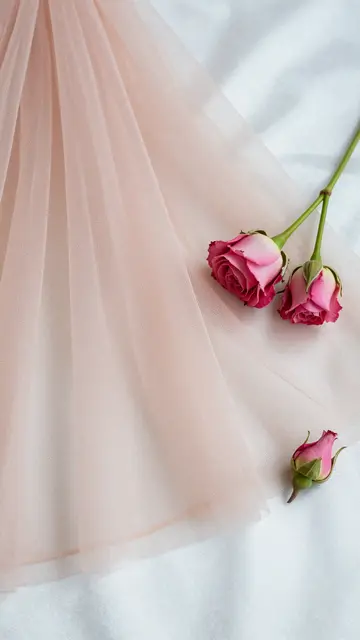 Delicate pink rosebuds rest atop soft blush tulle laid over ivory satin fabric.