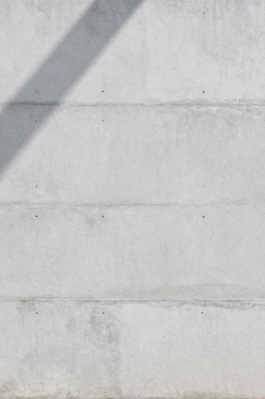 Light gray board-formed concrete wall with soft diagonal shadow across the upper left