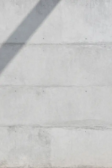 Light gray board-formed concrete wall with soft diagonal shadow across the upper left