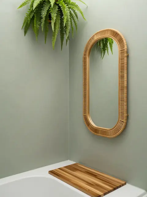 Sage plaster shower corner displays a scalloped rattan mirror, teak bath shelf and trailing overhead fern.