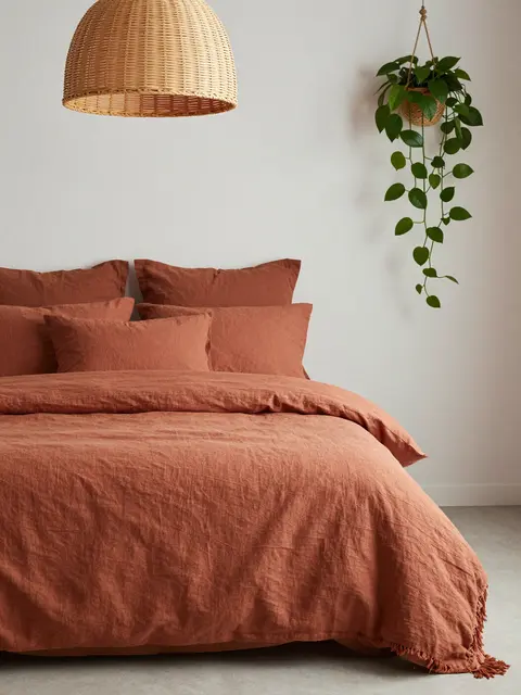 A boho bedroom with terracotta linen bedding, rattan pendant light, and hanging trailing pothos plant