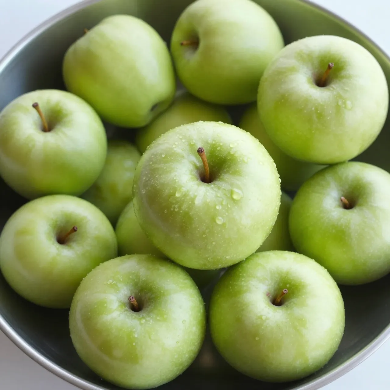 Top-down view of a bowl holding piled fresh, dewy green Granny Smith apples