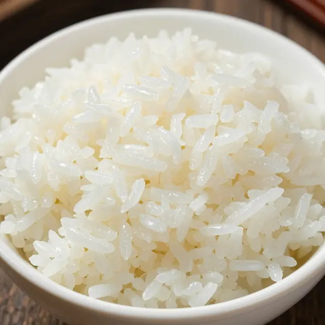 Close-up of fluffy cooked steamed white rice served in a white ceramic bowl on a dark wooden surface