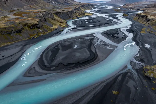Aerial view of turquoise glacial rivers winding across black volcanic sand in an Icelandic valley