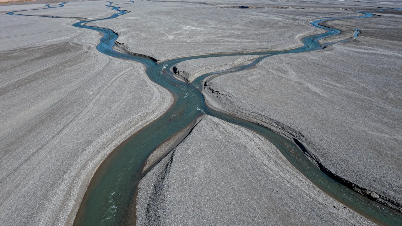 Aerial view of winding turquoise braided glacial river channels spreading across a wide gray gravel plain