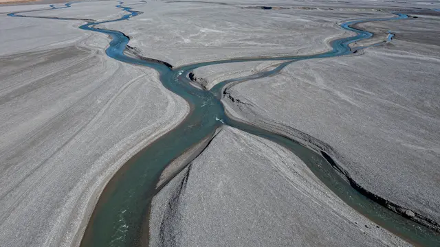 Aerial view of winding turquoise braided glacial river channels spreading across a wide gray gravel plain