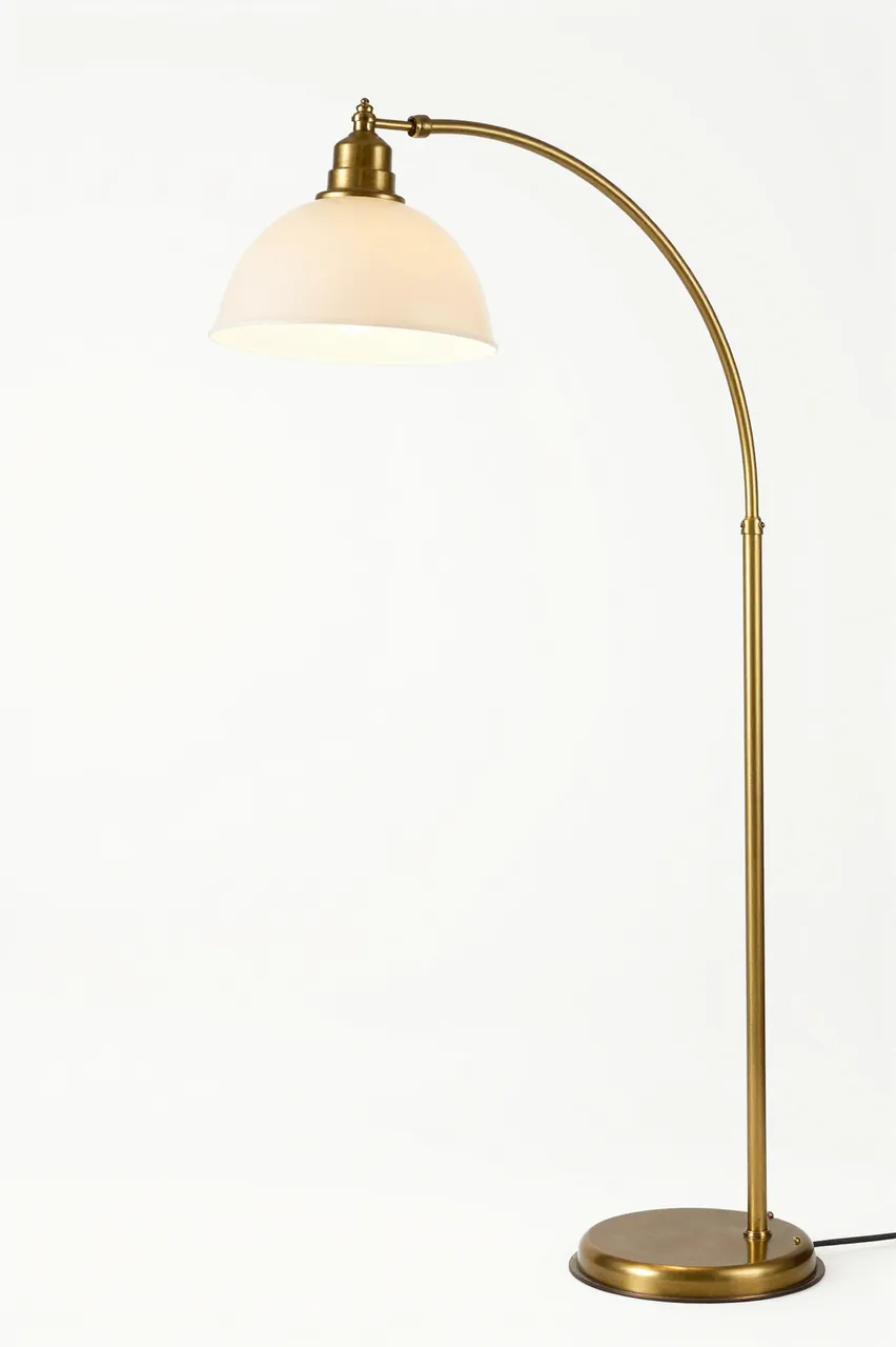 Brass arc floor lamp with a white dome shade stands against a plain white background