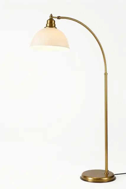 Brass arc floor lamp with a white dome shade stands against a plain white background