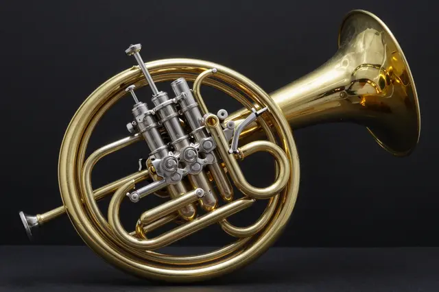 Polished brass french horn rests against a dark black studio background with dramatic lighting