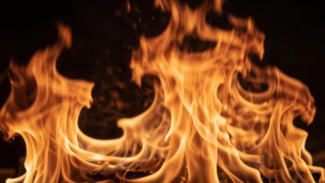 Swirling bright orange and yellow flames rise against a solid dark black background